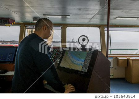Officer on watch with electronic chart on the navigational bridge. Caucasian man in blue uniform sweater using ECDIS on the bridge of cargo ship. Officer on watch with electronic chart on the navigational bridge. Caucasian man in blue uniform sweater using ECDIS on the bridge of cargo ship. 103643914