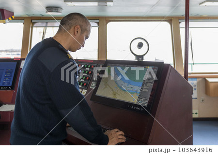 Officer on watch with electronic chart on the navigational bridge. Caucasian man in blue uniform sweater using ECDIS on the bridge of cargo ship. Officer on watch with electronic chart on the navigational bridge. Caucasian man in blue uniform sweater using ECDIS on the bridge of cargo ship. 103643916