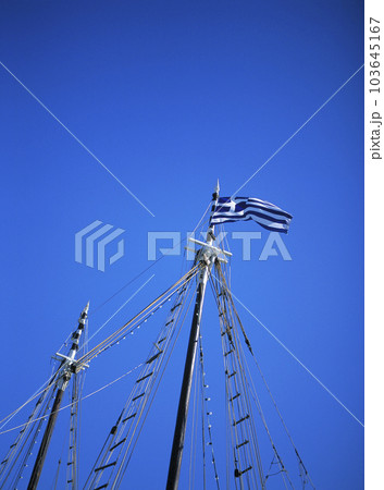 ミコノス湾に係留されたクルーザーヨットのマストに掲げられたギリシャの国旗 103645167