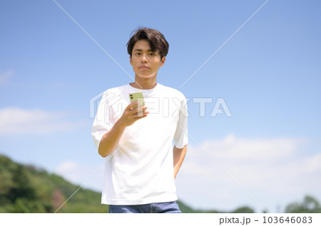 屋外でスマホを片手に持つ若い男性 103646083