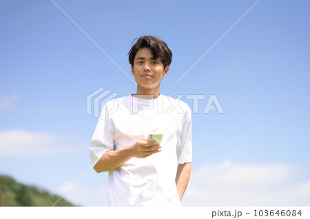 屋外でスマホを片手に持つ若い男性 屋外でスマホを片手に持つ若い男性 103646084
