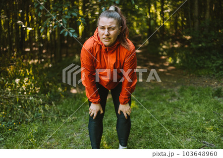 Tired female runner suffering with pain on sports running knee injury in nature. Person with backpack walking in the forest Tired female runner suffering with pain on sports running knee injury in nature. Person with backpack walking in the forest 103648960
