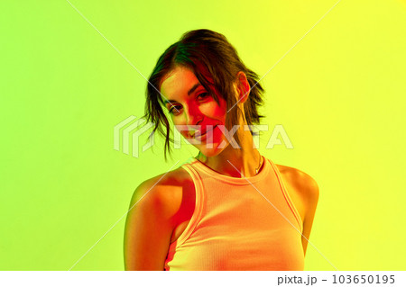 Portrait of charming girl, teenage, student with short hair smiling and posing with joyful face over yellow background in neon light 103650195