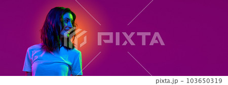 Portrait of young girl wearing white t-shirt looking away and smiling over pink color studio background in neon light. Banner with copy space for text Portrait of young girl wearing white t-shirt looking away and smiling over pink color studio background in neon light. Banner with copy space for text 103650319