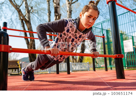 School physical education lessons. A caucasian teenage boy in a tracksuit is doing push-ups from the horizontal bar. Bottom view. Health and sport School physical education lessons. A caucasian teenage boy in a tracksuit is doing push-ups from the horizontal bar. Bottom view. Health and sport 103651174