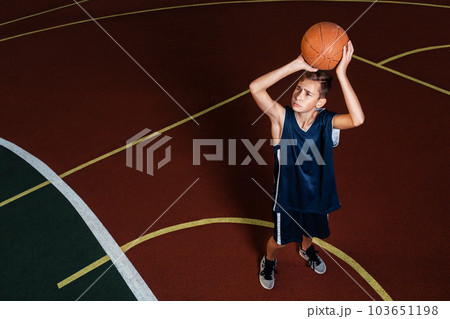 Sports and basketball. A young teenager in a blue tracksuit throws a jump ball into the basket. Ground on the background 103651198