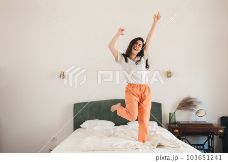 Happy young Caucasian woman dances on bed in bedroom. Freedom and winning Happy young Caucasian woman dances on bed in bedroom. Freedom and winning 103651241