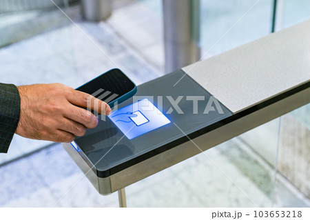 スマホをタッチしてエントランスゲートを通るビジネスパーソン スマホをタッチしてエントランスゲートを通るビジネスパーソン 103653218