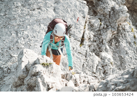 Looking down at woman climber wearing a protective helmet climbing up the mountain on a sunny day Looking down at woman climber wearing a protective helmet climbing up the mountain on a sunny day 103653424