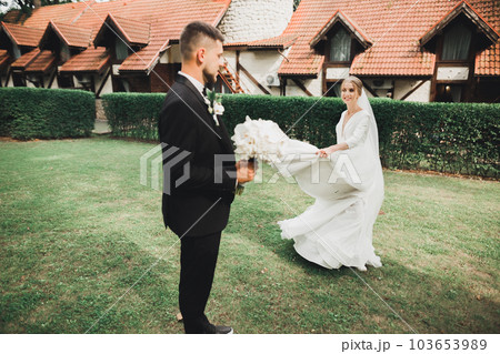 Stylish couple of happy newlyweds. Bride and groom in the park on their wedding day with bouquet 103653989