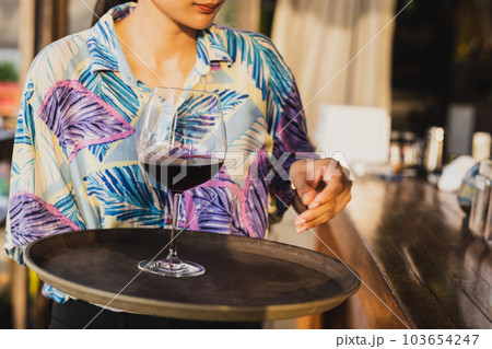 Waitress serving  glass of red wine on a tray. 103654247