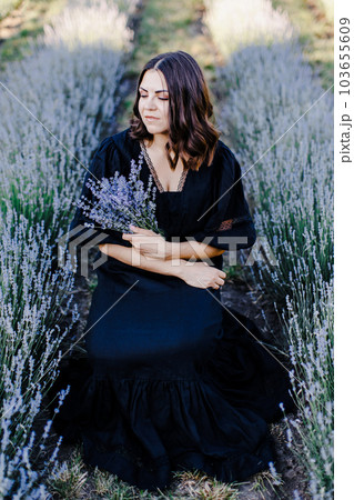 Attractive young woman in black dress standing surrounded by lavender field and holding bouquet with flowers Attractive young woman in black dress standing surrounded by lavender field and holding bouquet with flowers 103655609