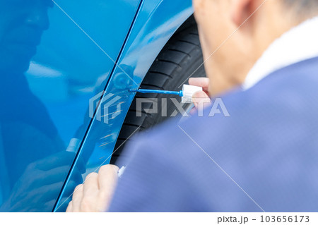 車についた擦り傷を自分で修理しようとしている中高年男性 車についた擦り傷を自分で修理しようとしている中高年男性 103656173