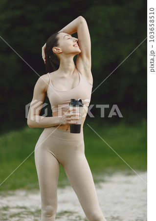 Pretty lady training on a summer sand. Brunette doing yoga. Girl in a sportsuit. 103658510