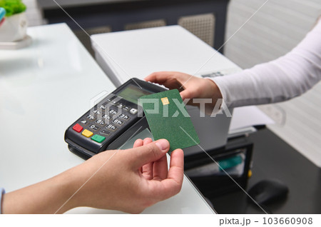Selective focus. Customer holding credit bank card with empty space for advertising text, over pos terminal reader, making wireless or cashless payment via NFC technology. Near field technology 103660908
