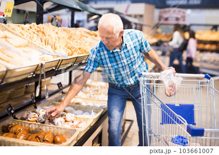 elderly man buying bread and pastries in grocery section of the supermarket elderly man buying bread and pastries in grocery section of the supermarket 103661007