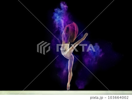 Young girl, flexible ballerina in beige bodysuit standing on pointe, dancing with colorful powder against black studio background 103664002
