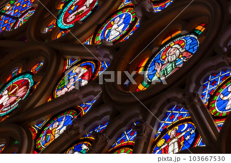 Medieval era rose window stained glass panels showing saints, angels set in stone gothic tracery in a cathedral.  103667530