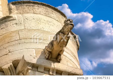 Detail of stone carved gargoyle on a stone tower. View from below. Blue sky, clouds in background. High quality photo 103667531