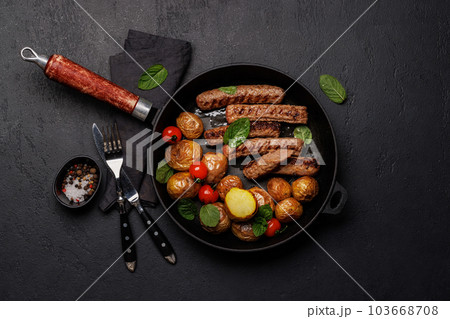Delicious grilled sausages and potatoes in a sizzling frying pan 103668708