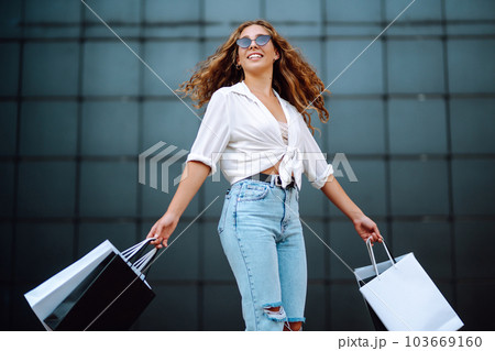 Young woman with shopping bags walking on street. Summer shopping. Sale, shopping, lifestyle concept Young woman with shopping bags walking on street. Summer shopping. Sale, shopping, lifestyle concept 103669160