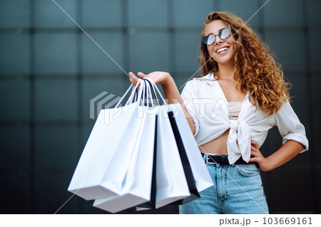 Young woman with shopping bags walking on street. Summer shopping. Sale, shopping, lifestyle concept Young woman with shopping bags walking on street. Summer shopping. Sale, shopping, lifestyle concept 103669161