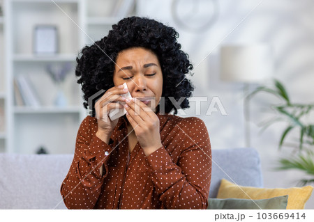 Portrait of a young African American woman at home crying, wiping tears with a napkin, suffering from depression, received bad news about death. He has health problems and financial problems. 103669414