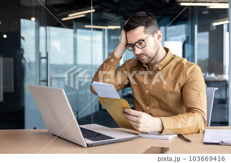 A worried young man, a businessman, an accountant works in the office, received a letter with accounts, credit, debt, a notice of bankruptcy. He holds his head in shock, thinks about solving the 103669416