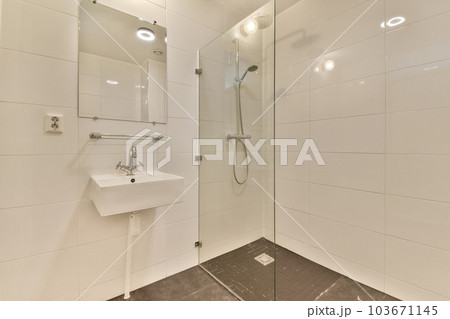 a modern bathroom with white tiles and marble flooring, including a glass shower stall on the right hand side 103671145
