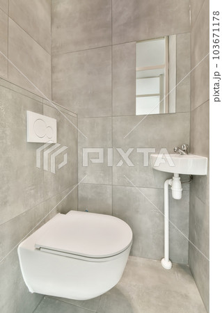 a white toilet and sink in a bathroom with grey tiles on the wall behind it, there is a mirror 103671178