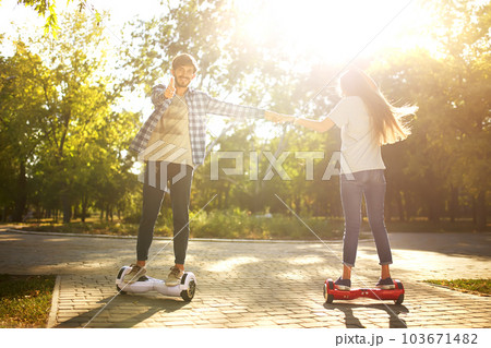 Young man and woman riding on the Hoverboard in the park. content technologies. a new movement. Young man and woman riding on the Hoverboard in the park. content technologies. a new movement. 103671482
