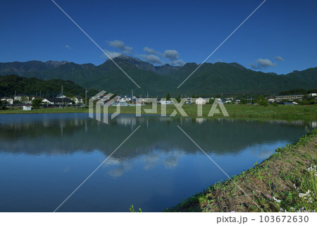 北杜市白州町、田植え待つ水面に映る南アルプスの山並みと麓の街並み 103672630