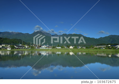北杜市白州町、田植え待つ水面に映る南アルプスの山並みと麓の街並み 103672675
