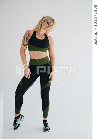 an attractive blonde in a black and green tracksuit poses on a white background. an attractive blonde in a black and green tracksuit poses on a white background. 103672808