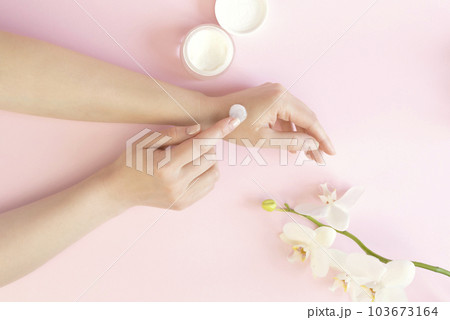 Well-groomed female hands with cosmetic cream on a pink background. A sprig of orchid and a jar of cream. 103673164