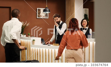 Professional concierge personnel welcoming tourists at reception desk during check in process. Elegant friendly receptionist team greeting vacation trip guests in hotel lobby 103674764