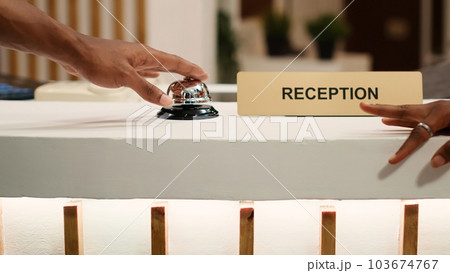 Close up of african american guests ringing service bell at reception desk, ready to book in their room reservation. Concierge receptionists typing data during tourists check in process 103674767