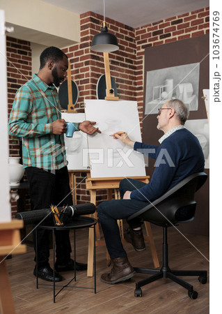 Senior man attending art classes interacting with other students and teachers during drawing lesson, people learning something new in retirement. Creative team building activities 103674769