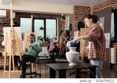 Young woman teacher having drawing lesson in art school, teaching different aged people to draw. Group of diverse students learning sketching techniques. Creative activities for adults 103674813