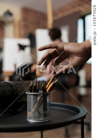 Close up of male hand taking pencil out of metal cup holder during drawing lesson, selective focus. People learning to draw and sketch at group art class, sketching tools and supplies 103674826