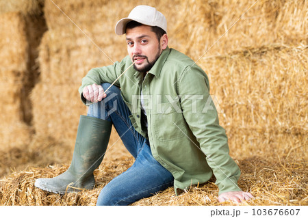 Male farmer posing against the background of hay bales in hayloft 103676607