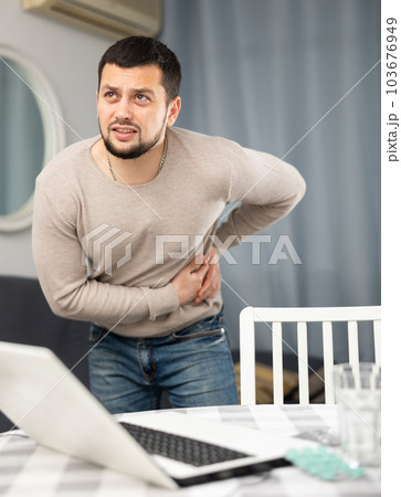 Man experiences severe pain in his side, the fruit of prolonged work on laptop at home 103676949