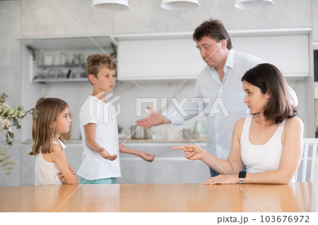 At home in kitchen, outraged mom and dad scold their son and daughter for disobedience. 103676972