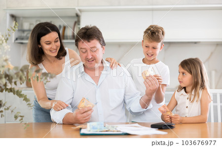 Adult man sitting at table distributes money to family 103676977