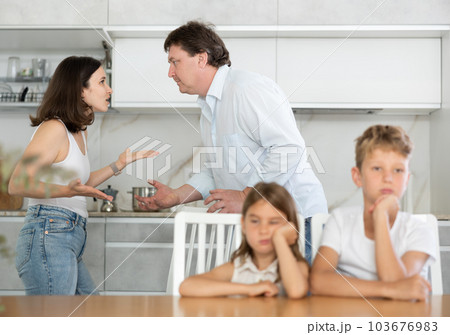 Brother and sister sit at table during quarrel between parents 103676983
