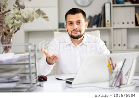 Positive man office worker sitting at table and gesturing 103676984