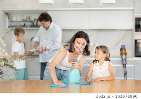 Little girl helps mother wash kitchen table. 103676990