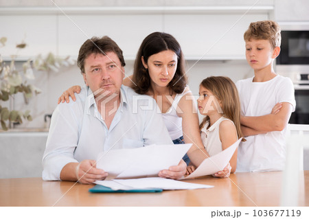 Wistful father looking through papers with family Wistful father looking through papers with family 103677119