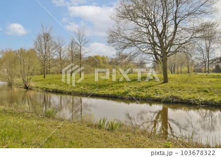 a river with trees and grass in the foregrounds are reflected in the water, on a sunny spring day 103678322