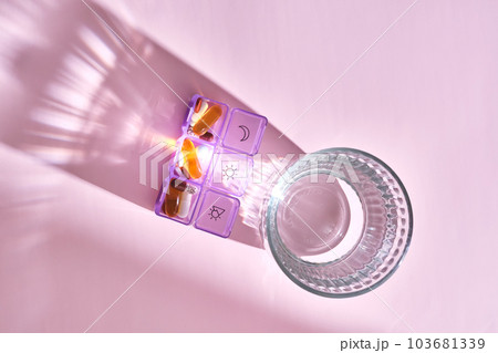 Bright pill box with different pills and vitamins next to a glass of water. Bright pill box with different pills and vitamins next to a glass of water. 103681339